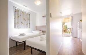 Ein Zimmer mit zwei Betten, einem Vorhang vor dem Fenster, Holzboden und Blick ins Freie.
