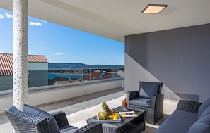 Ein Balkon mit Korbmöbeln, einem Tisch mit Früchten und Getränken und Blick auf die Küste.