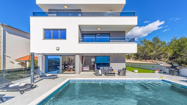 Una casa moderna de dos pisos amb piscina, zona d'estar a l'exterior i un balcó.
