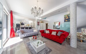Ein großzügiger Wohnbereich mit einem roten Sofa, einem grauen Sofa, einem Glastisch und einer Chandelier.