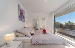Ein modernes Schlafzimmer mit Bett, Nachttischlampe, großem Fenster und angrenzendem Badezimmer.