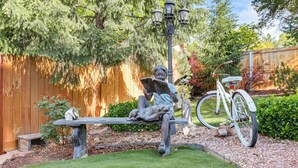 Una estatua de jardín de un niño leyendo, una bicicleta y una valla de madera.