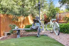 Eine Gartenstatue eines Kindes beim Lesen, ein Fahrrad und ein Holzzaun.