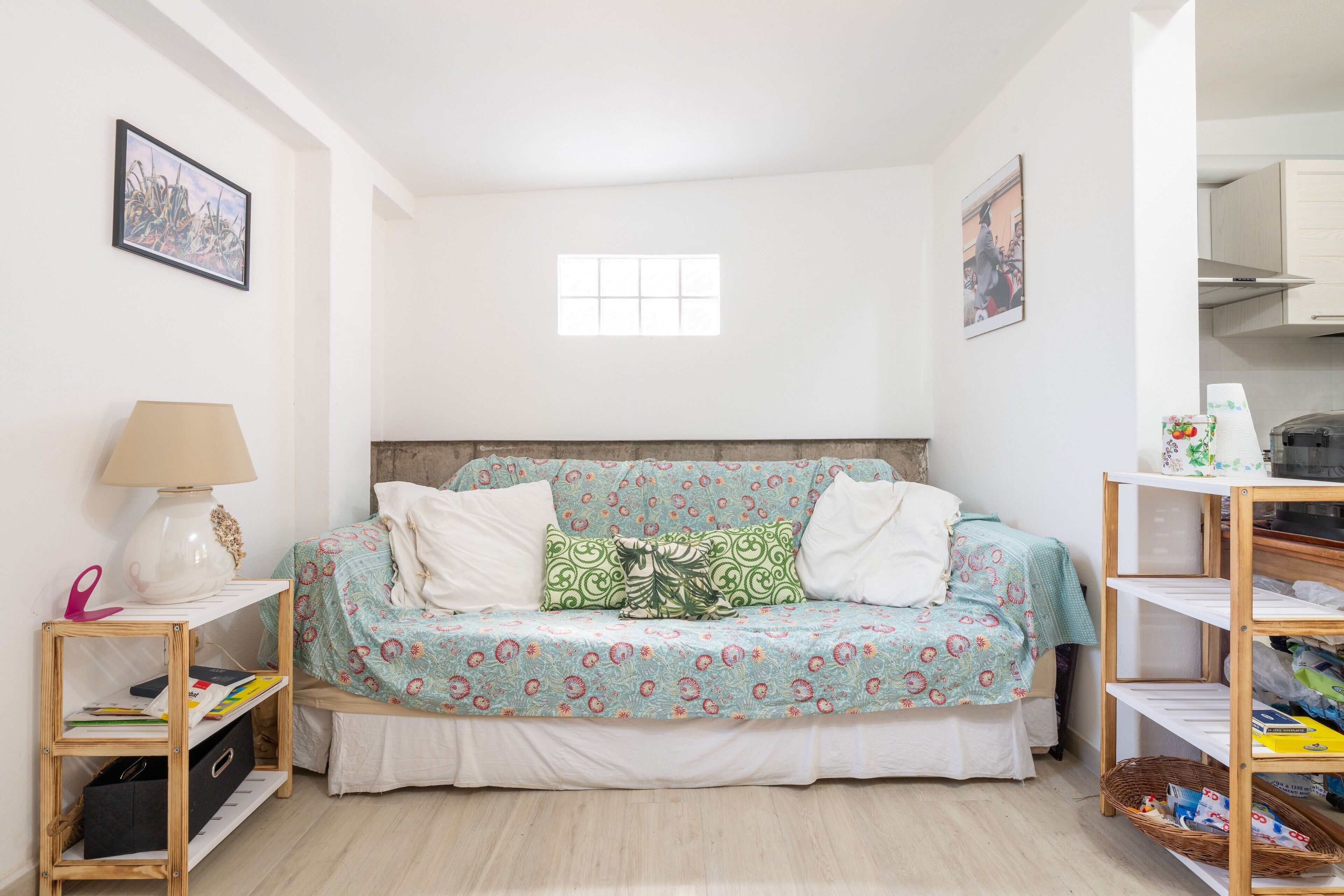 A bedroom with a bed, a bedside table, a lamp, a shelf, and a window.