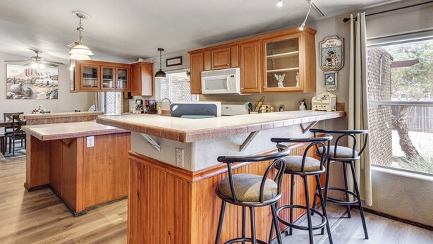 A kitchen with wooden cabinets, a microwave, and a bar area with stools. - 7 Miles to Roosevelt Lake! Mtn-View Family Escape (Tonto Basin)