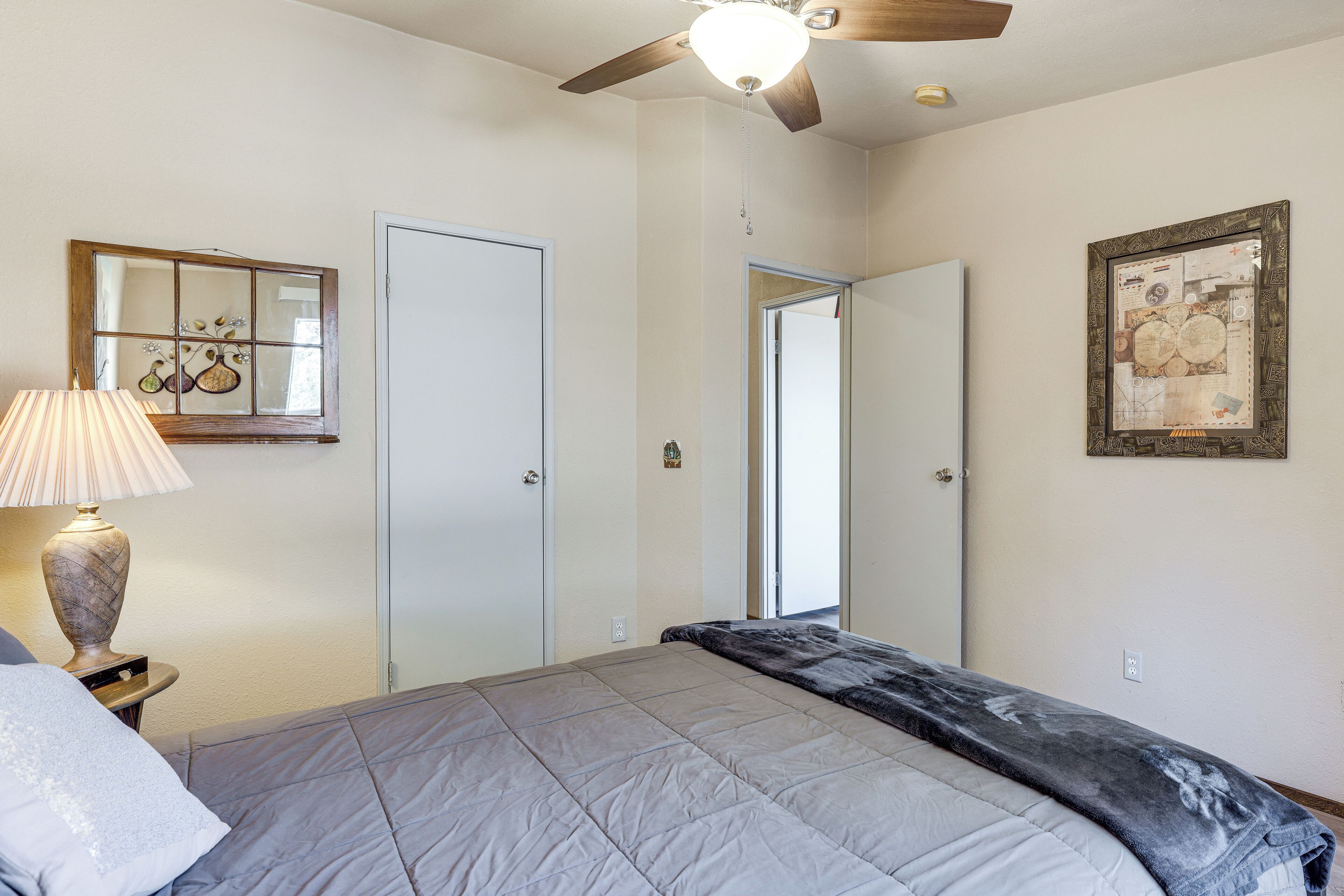 Un dormitorio con cama, ventilador de techo, lámpara, espejo y un cuadro en la pared.