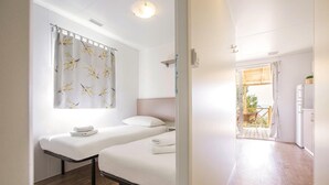 Une chambre avec deux lits, une fenêtre avec un rideau, un plancher en bois et une vue sur l’extérieur.