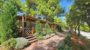 Une rangée de cabanes en bois, reliées par un chemin pavé de briques, et entourées d’arbres.