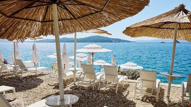Un salon de plage doté de chaises longues blanches et de parasols en chaume, offrant une vue sur une mer calme.