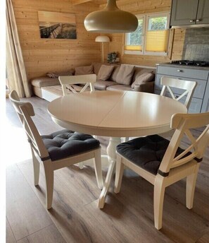 A wooden interior with a round dining table, cushioned chairs, a pendant light, and a kitchen area. - Holiday home in Menaldum with swimming pool (Menaldum)