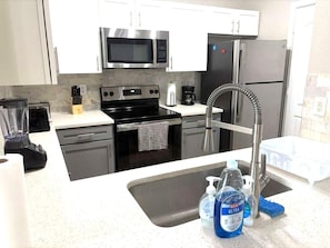 A modern kitchen with stainless steel appliances, a dishwasher, a coffee maker, and a sink with hand soap. - Sunny 2BR Magnolia Escape Pool, Gym & Location (Magnolia)