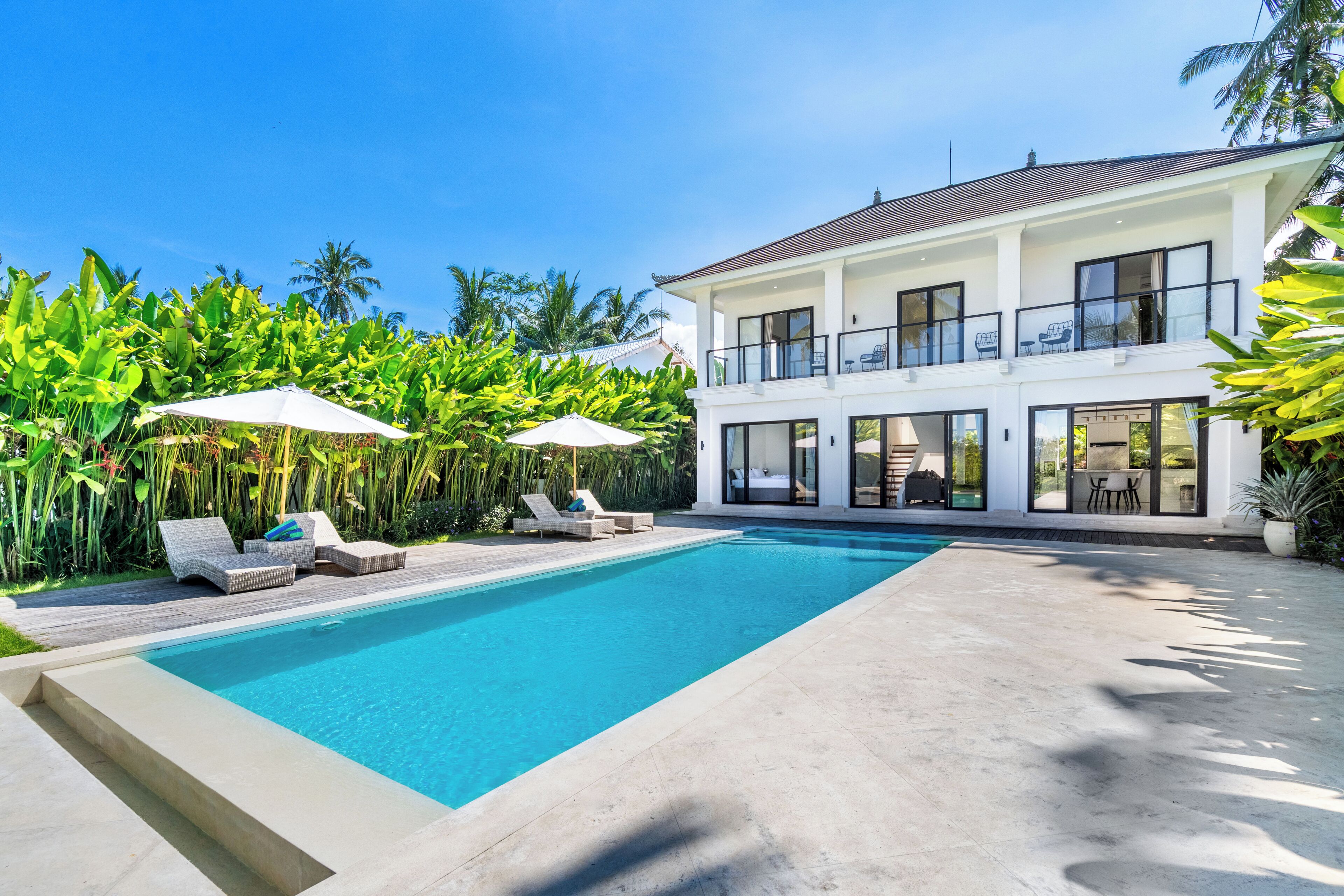 A two-story house with a swimming pool, outdoor seating, and lush greenery.