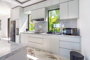Cocina moderna con armarios blancos, refrigerador de acero inoxidable, microondas y ventana con vistas a zonas verdes.