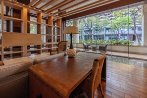 Ein modernes Interieur mit einem Holztisch, gepolsterten Sitzmöglichkeiten, einer Lampe und Blick durch große Fenster.