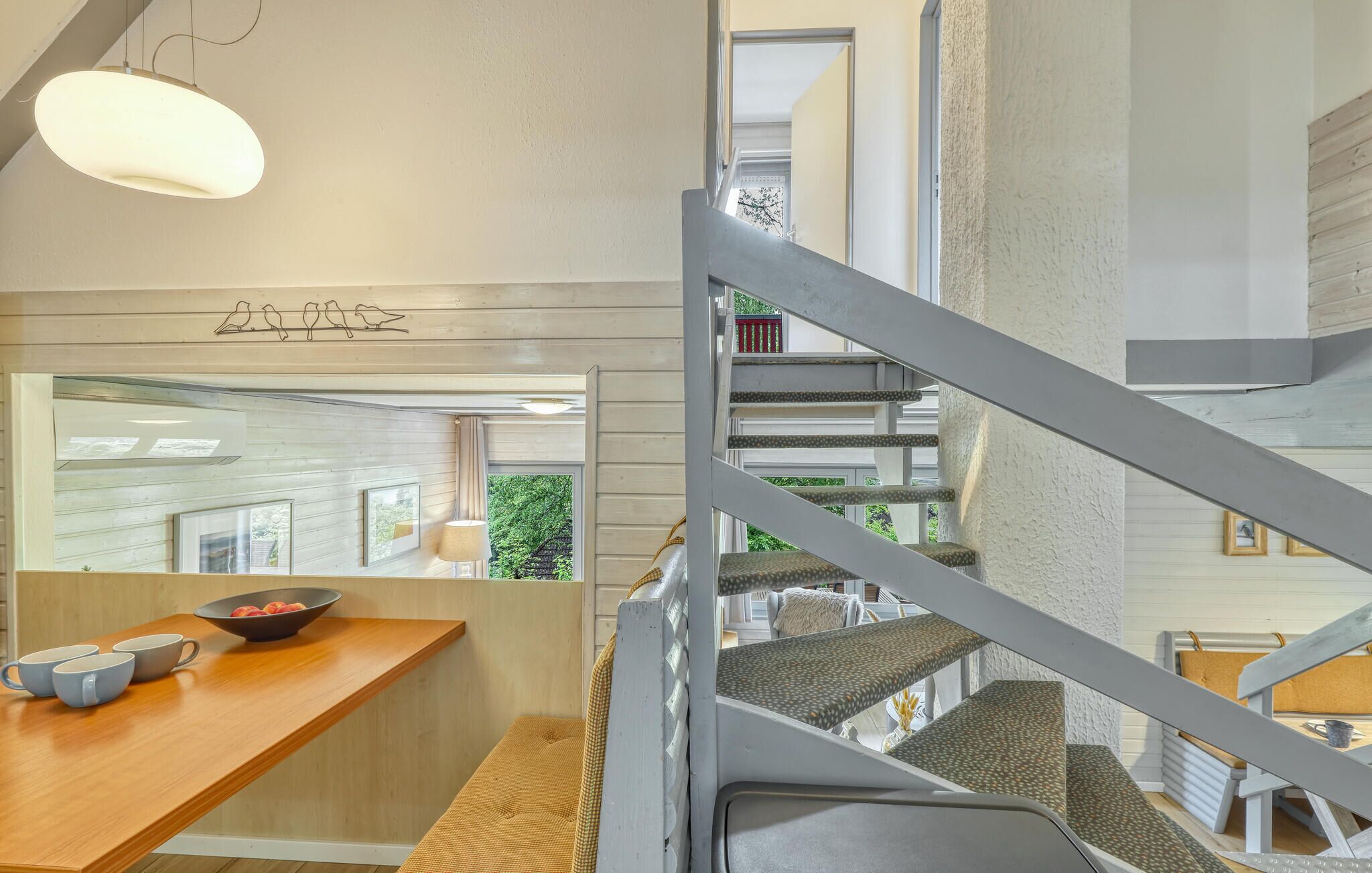 Eine moderne Küche mit Holzarbeitsplatte, einer hängenden Leuchte und Blick auf eine Treppe, die zu einer oberen Ebene führt.