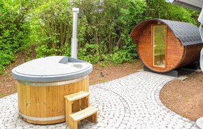 Ein hölzernes Whirlpool mit Treppe, eine Holzaus und ein gepflasterter Weg in einem bewaldeten Gebiet.