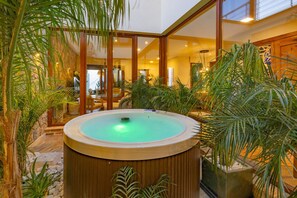 Ein Whirlpool, umgeben von Pflanzen, in einem gut beleuchteten Innenraum mit Holzboden und einem großen Fenster.