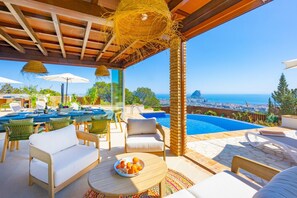 Ein Poolbereich mit Sitzgelegenheiten im Freien, Blick auf das Meer und eine Stadtkulisse im Hintergrund.