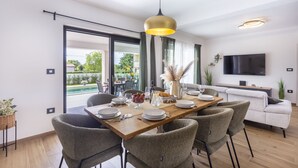 A modern dining area with a wooden table, grey upholstered chairs, and a large window with a view of greenery.