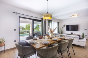 A modern dining area with a wooden table, grey upholstered chairs, and a large window with a view of greenery. - Completely new!!!! Exclusive villa with 4 bedrooms and a private 32 m² pool (ŽMINJ)
