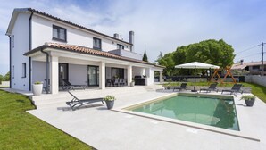 A modern house with a swimming pool, outdoor seating, and a covered patio.