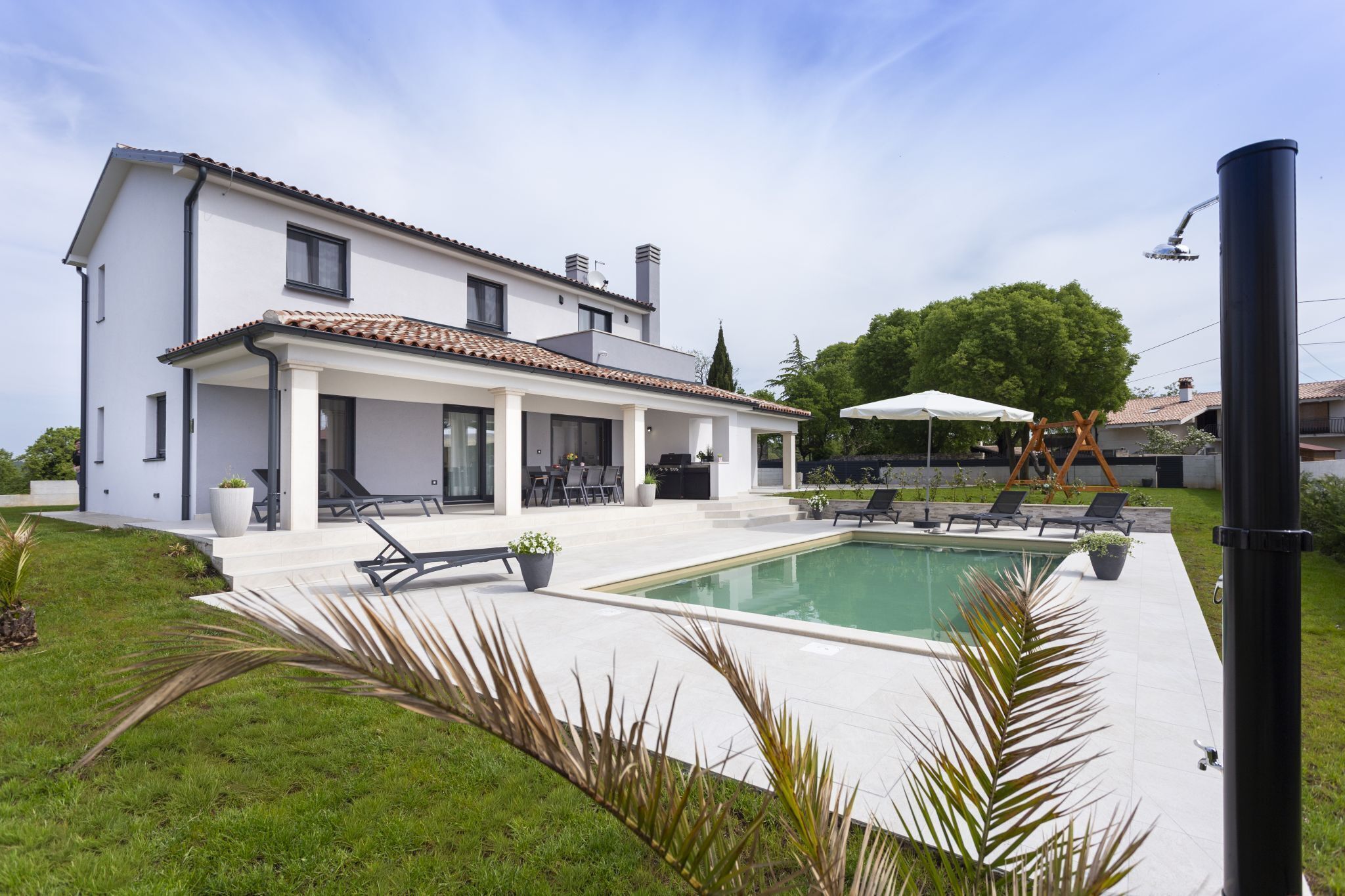 Una moderna casa a due piani con piscina, area salotto esterna e patio coperto.