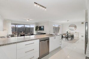 A modern kitchen with a large island, built-in appliances, and a dining area with a round table and chairs. - The Grand Aveley House (Aveley)
