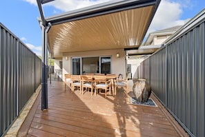 A covered outdoor patio with a wooden table and chairs, a large vase, and a metal fence. - The Grand Aveley House (Aveley)