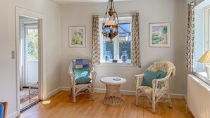 Una habitación con dos sillones de mimbre, una mesita redonda pequeña, una lámpara colgante y dos cuadros enmarcados en las paredes.