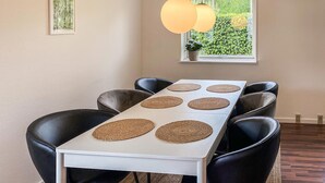 Un coin repas avec une table blanche, des chaises noires et des sets de table en fibres tressées.