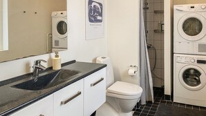 Une salle de bain équipée d’un lavabo, d’un miroir, de toilettes et de machines à laver superposées.