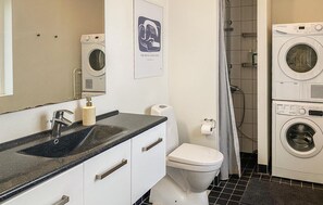Un baño con lavamanos, espejo, inodoro y lavadoras apiladas.