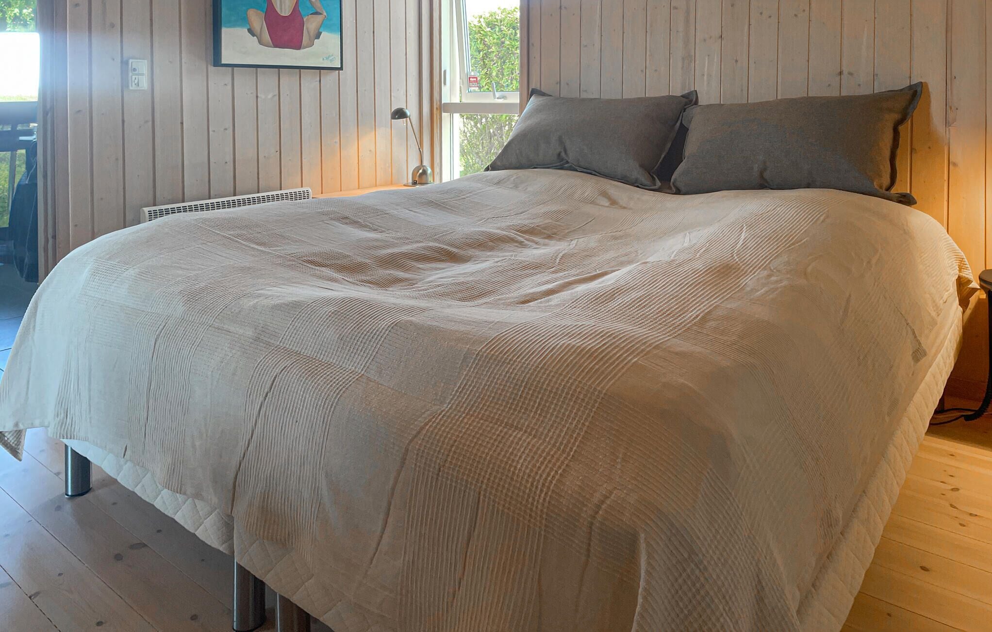 Ein Bett mit weißer Strukturdecke, ein Fenster mit Blick auf Grünflächen und ein Bild an der Wand.
