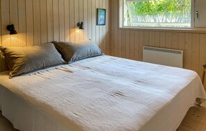 A bed with a white bedspread, two pillows, a wall-mounted lamp, a framed picture, and a window with a view of trees. - Beautiful home in Fårevejle with house sea view (Fårevejle)