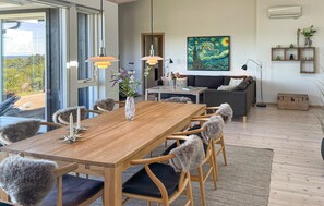 A modern living room with a wooden dining table, grey furry chairs, a grey sofa, a painting on the wall, and a view through a glass door. - Beautiful home in Fårevejle with house sea view (Fårevejle)
