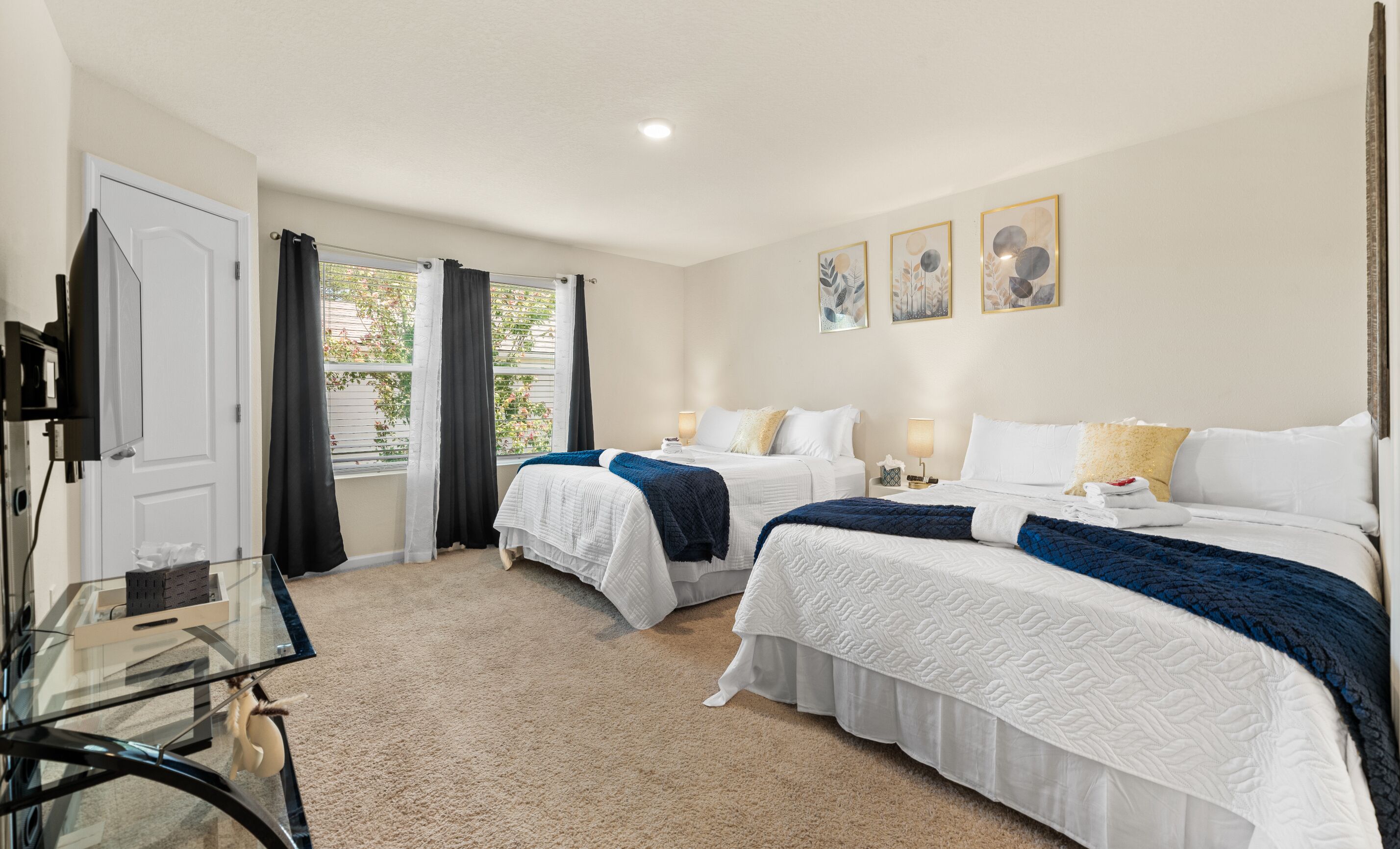 A hotel room with two beds, a TV, a glass table, and a window with curtains.