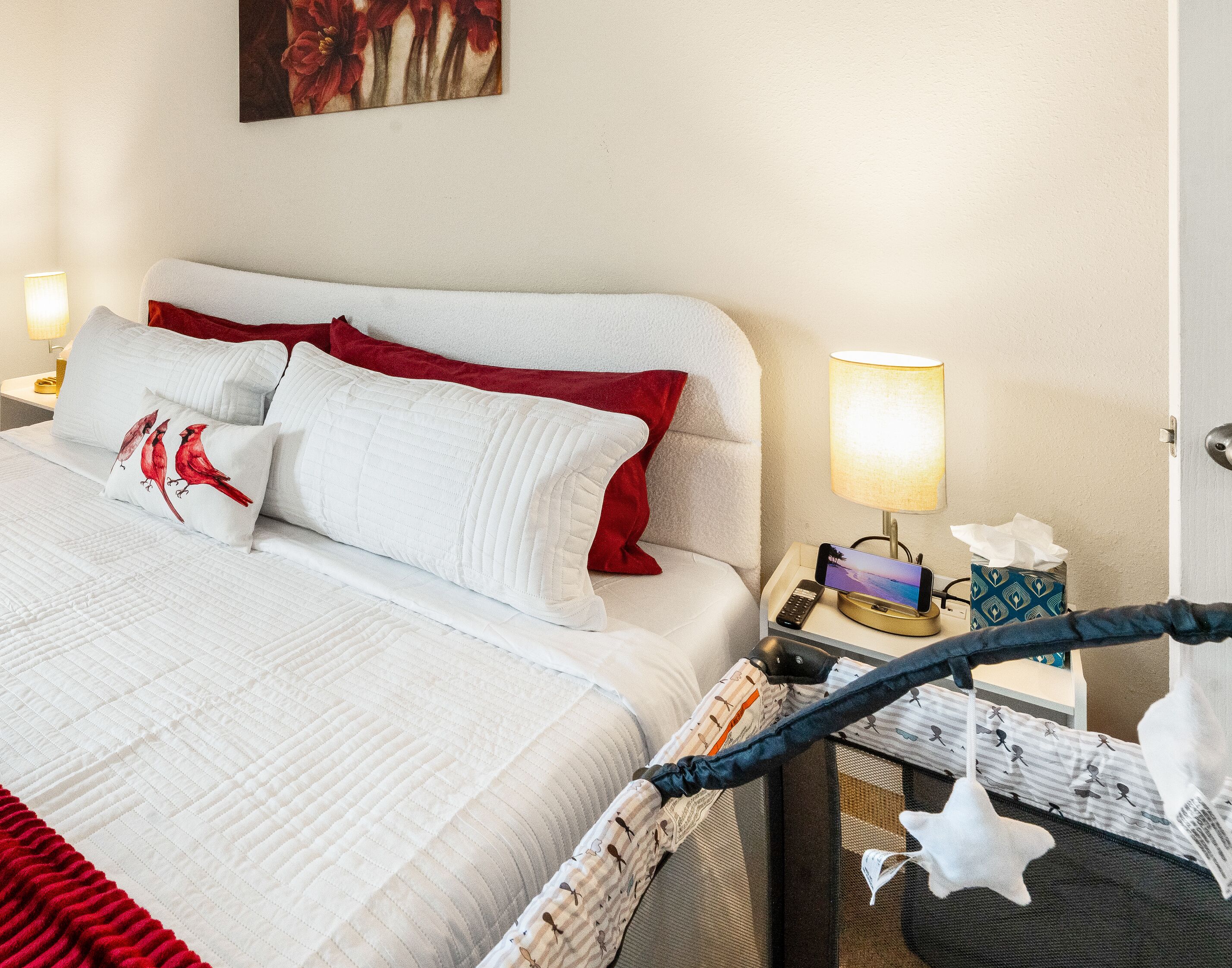 A neatly made bed with pillows, a bedside lamp, a phone charging station, and a small table with a tissue box.