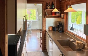 A kitchen with a coffee maker, a sink, and a window with a view of greenery. - 3 bedroom cozy home in Kalundborg (Kalundborg)