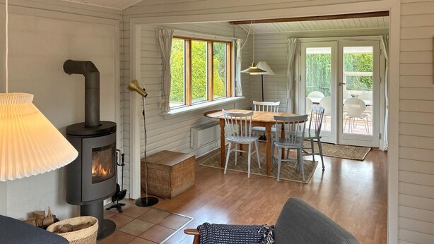 Ein gemütliches Zimmer mit Kamin, einem Esstisch mit Stühlen, einer Couch und Blick durch große Fenster.