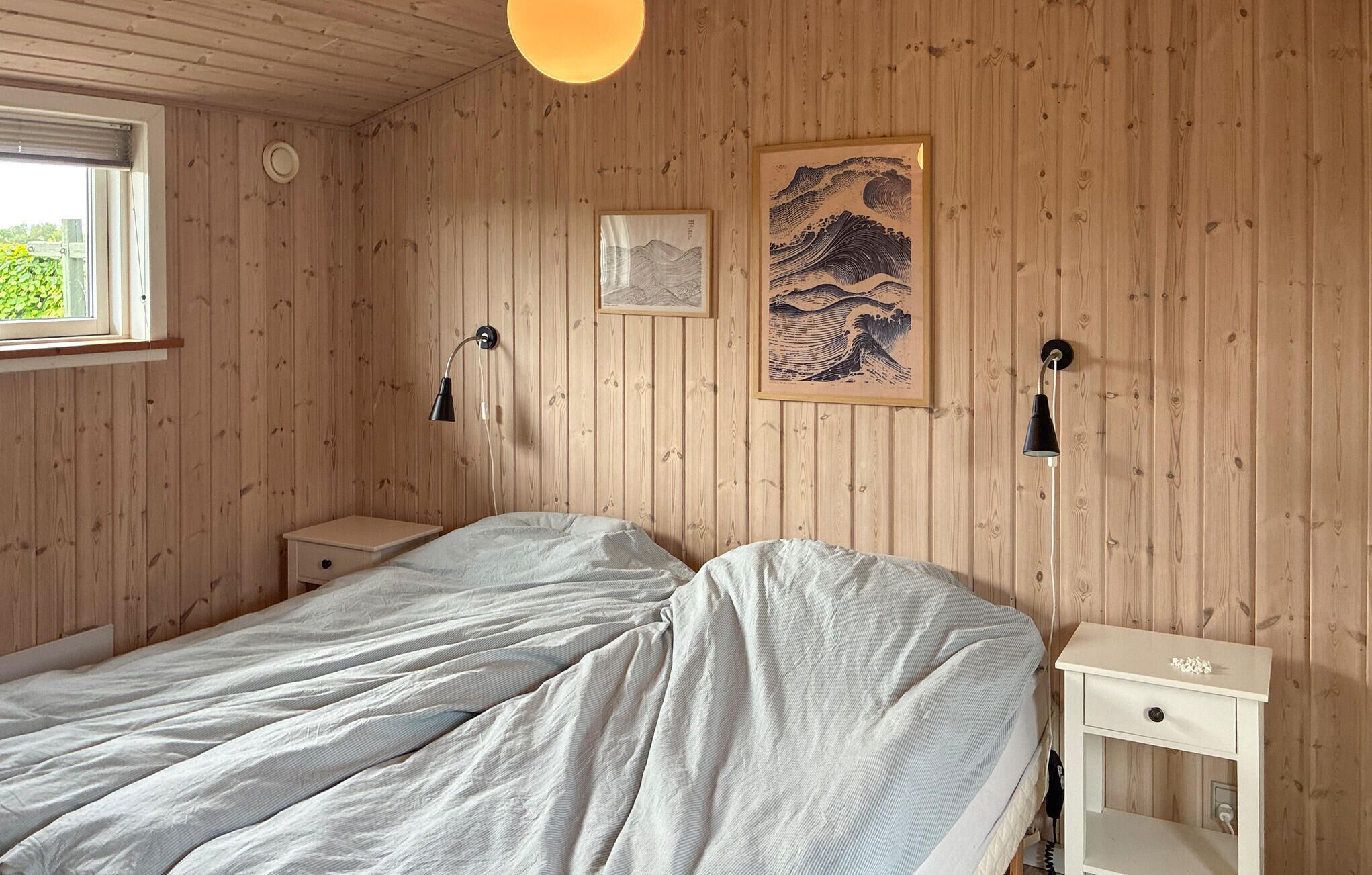 A room with wooden walls, two beds with white linens, two bedside tables, and two wall-mounted lamps.