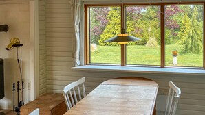 Ein Holztisch mit weißen Stühlen, ein Fenster mit Vorhängen und eine Hängelampe.