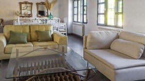 Een woonkamer met een glazen salontafel, twee banken, een eethoek met een witte tafel en stoelen, en grote ramen met natuurlijk licht.