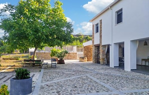 A courtyard with stone flooring, a tree, benches, and a building with stone walls and windows. - Beautiful home in Alcala la Real (Alcala la Real)