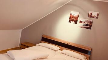 A neatly made bed with white linens in a room with a sloped ceiling and wooden headboard. There are three framed pictures on the wall above the bed.