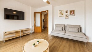 A living room with a sofa, TV, wooden floor, ceiling fan, and wall art. - 2 bedroom awesome apartment in Benicasim (Benicasim)