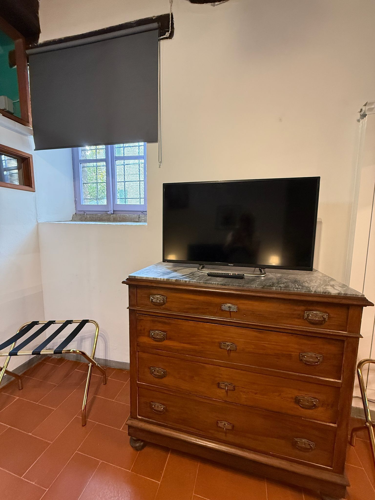 Ein Zimmer mit Fernseher auf einer Holzkommode, einem Fenster mit Blick und einem Metallstuhl.