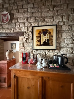 Eine rustikale Küche mit einer Steinwand, einem gerahmten Bild eines Gebäudes, einer Kaffeemaschine und verschiedenen Küchenutensilien auf der Arbeitsfläche.