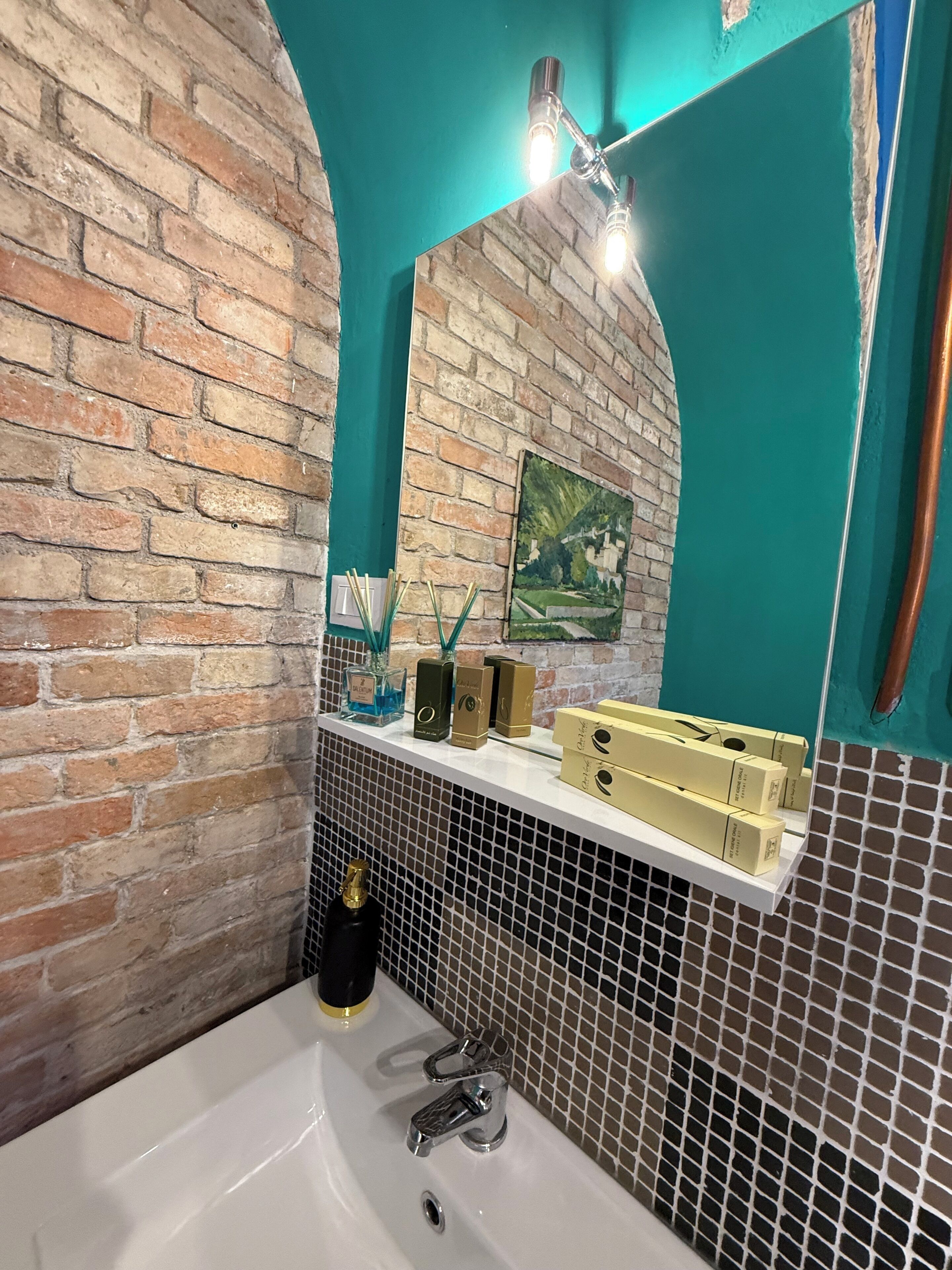 A bathroom with a brick wall, a white sink, a mirror, and a shelf with toiletries.