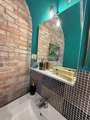 Ein Badezimmer mit Backsteinwand, einem weißen Waschbecken, einem Spiegel und einem Ablagefach mit Toilettenartikeln.