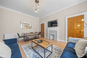 A living room with a sofa, a coffee table, a fireplace, a television, and a dining area. - Castle Terrace: Stylish Victorian Townhouse in the Heart of Stirling (Stirling)